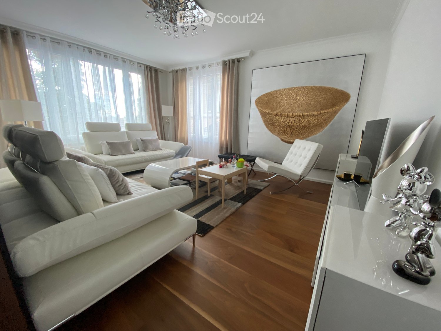 Modern living room with white leather sofas, a coffee table, a small side table, a hanging woven basket, and a decorative sculpture on a console table.