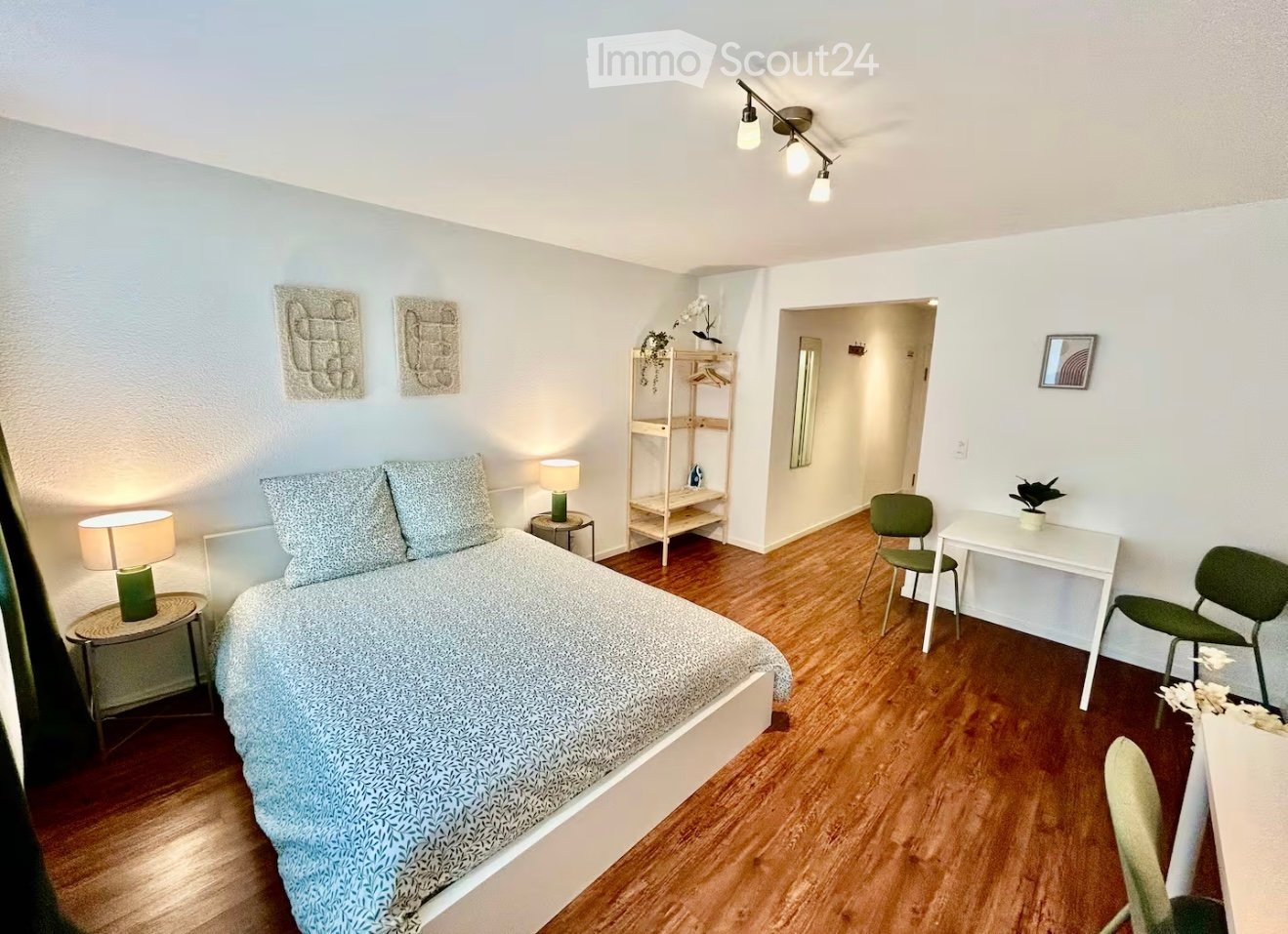 Cozy bedroom with a double bed, nightstands, lamps, a small table with chairs, a shelf, and a mirror in the adjacent hallway.