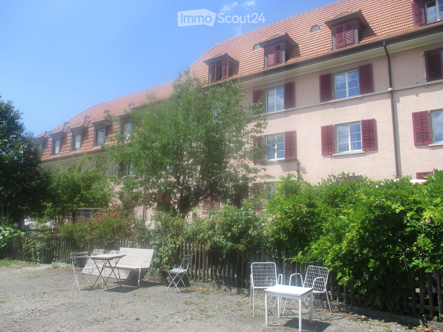 3 story building, red roof, red shutters, white walls, garden, outdoor seating
