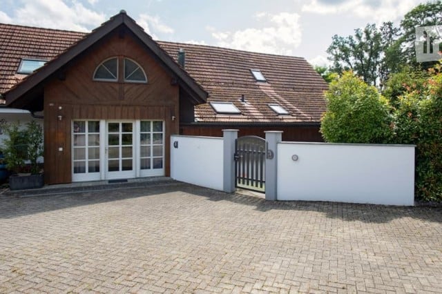Two-story house with a wooden facade, red-tiled roof, large garage, and a gated driveway.
