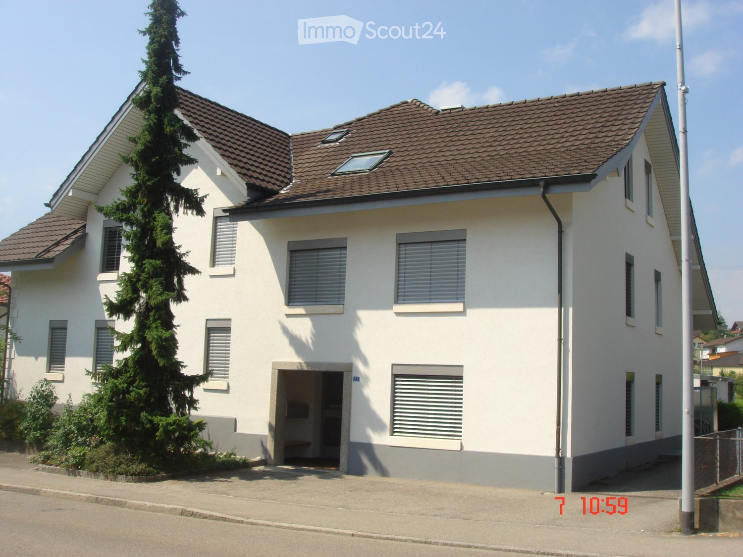 Two-story house with white walls, brown tiled roof, multiple windows with shutters, and a small front entrance.