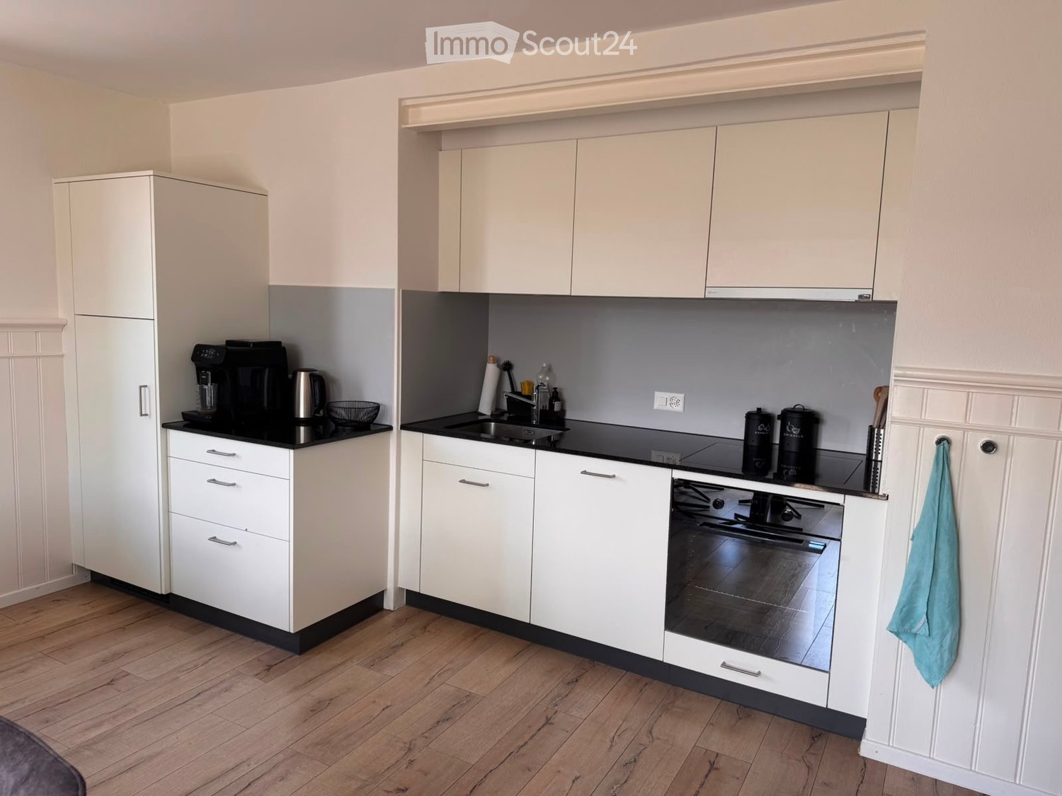 Modern kitchen with white cabinets, black countertops, and stainless steel appliances, including a coffee maker, oven, and sink.