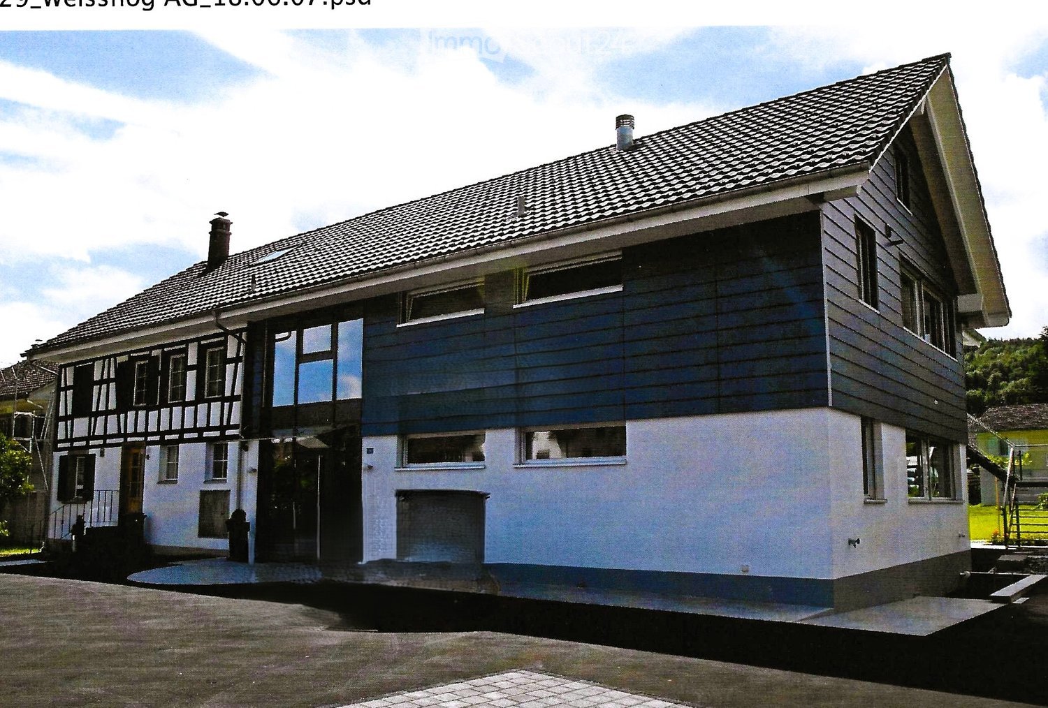 Two-story house with a combination of dark blue and white exterior walls, multiple windows, and a tiled roof. Features a raised ground floor and a small garage.