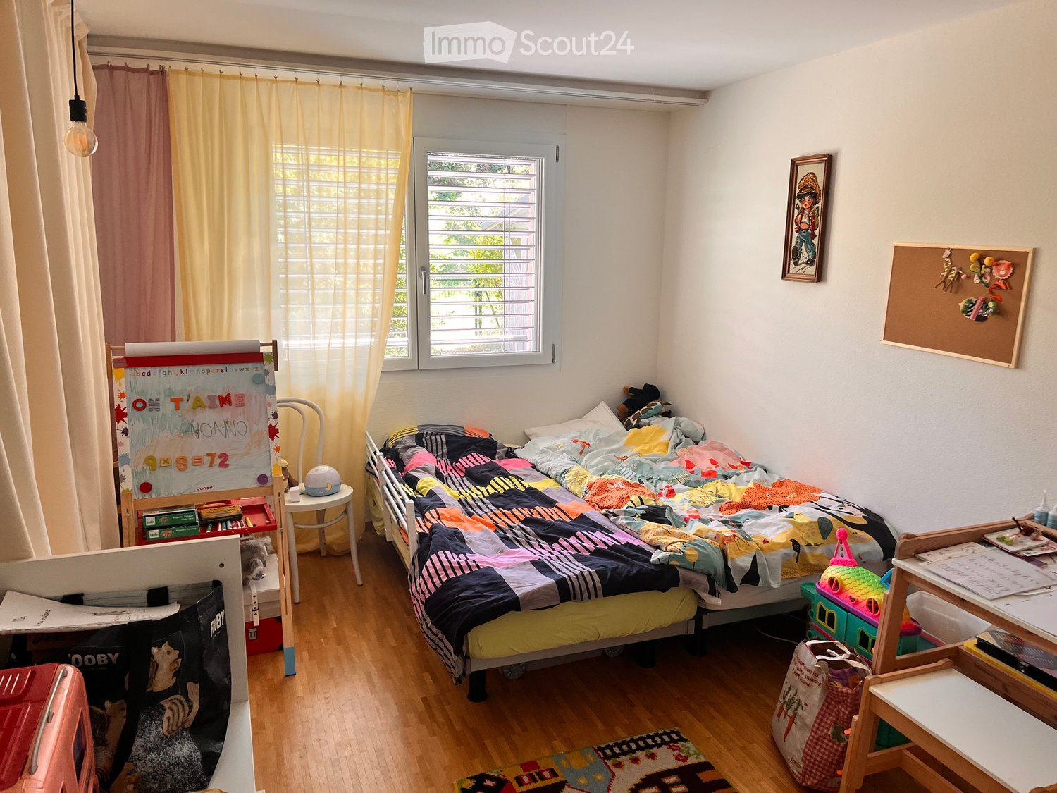A cozy children's bedroom with a single bed, colorful quilt, small table, chair, and various toys and decorations.
