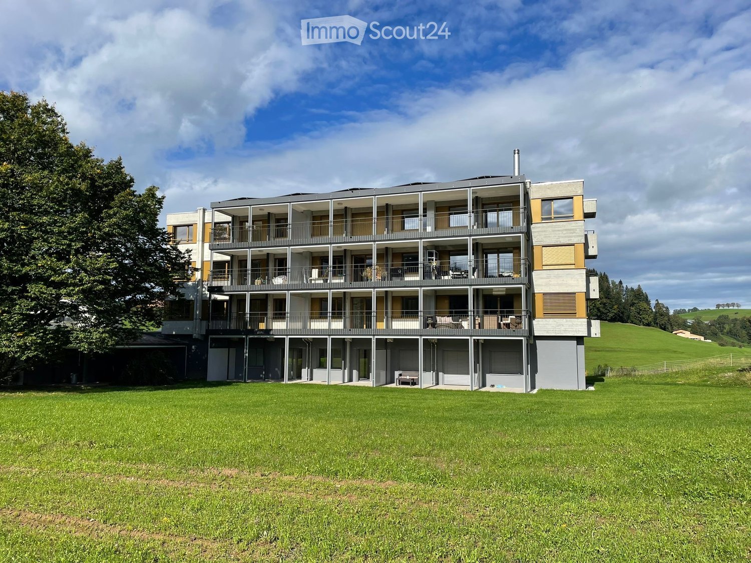modern apartment building, 3 floors, multiple balconies, large green field in front