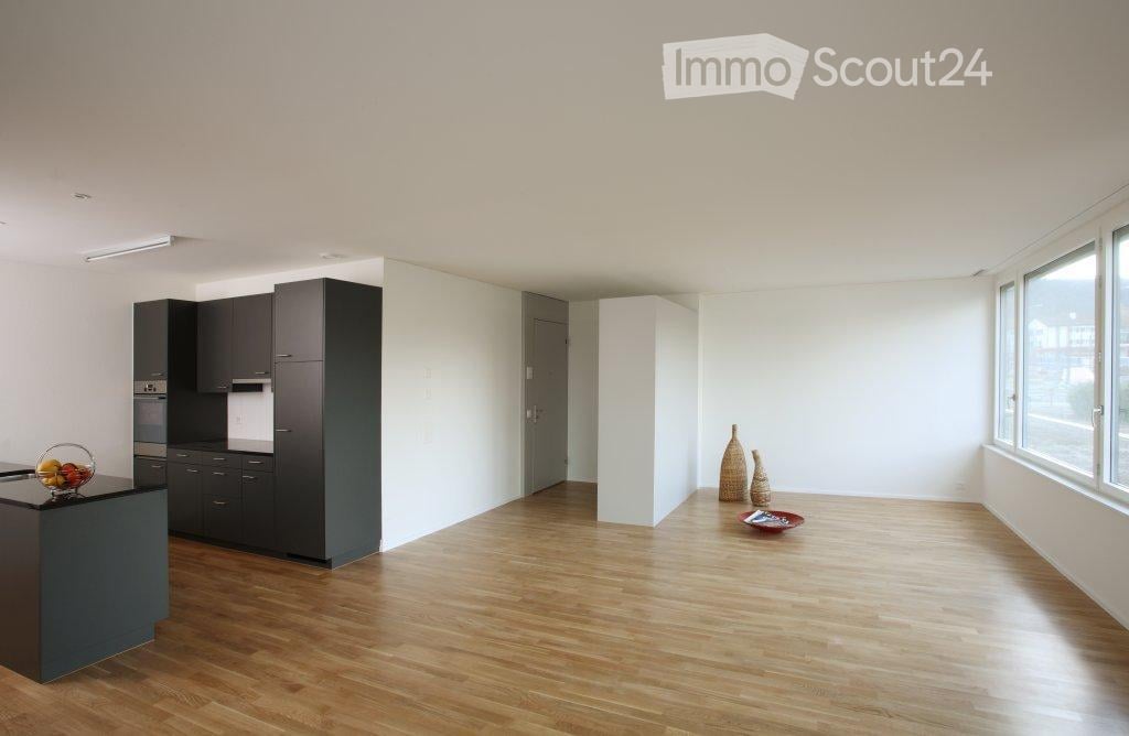 Modern kitchen with dark cabinets, light wooden flooring, and large windows. Includes a countertop with a bowl of fruit, vases, and a small decorative bowl.