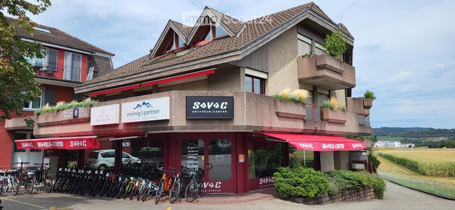 A two-story building with a red awning and signage for "SAVC Ski & Velo-Center" and "Minning & Partner" law office. The storefront displays multiple bicycles lined up outside.