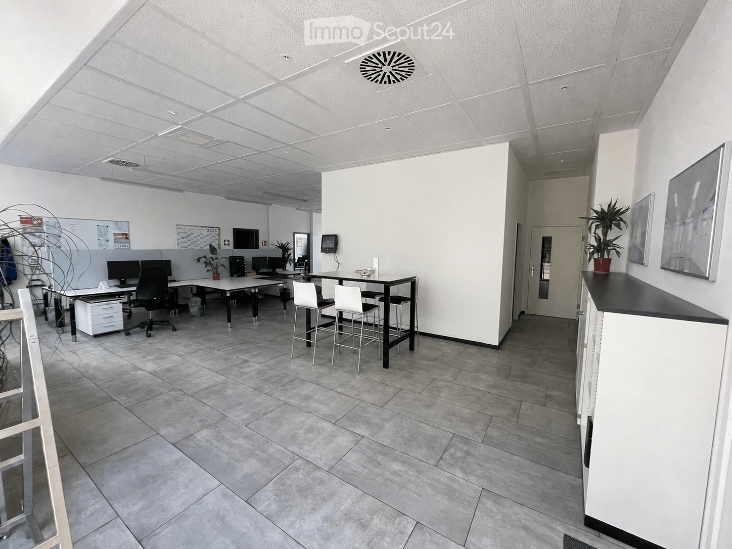 Office space with tiled floor, white walls, and modern furniture including chairs, stools, tables, and screens.