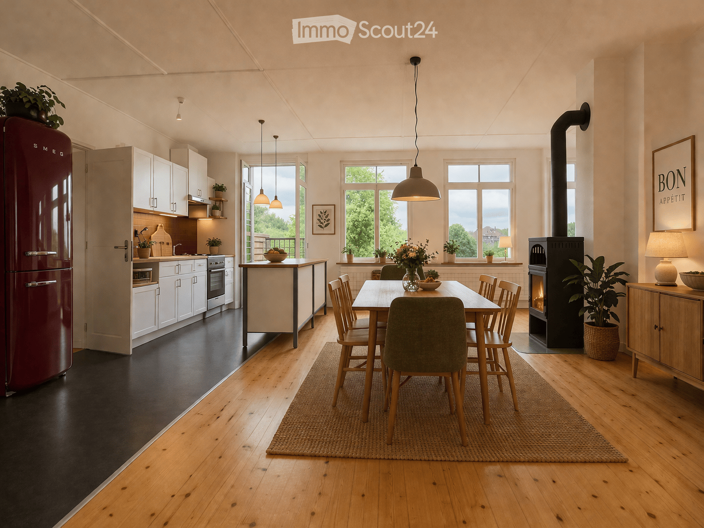 Open-plan kitchen and dining area with white cabinets, a red refrigerator, a central dining table with chairs, a wood-burning stove, pendant lights, and potted plants.