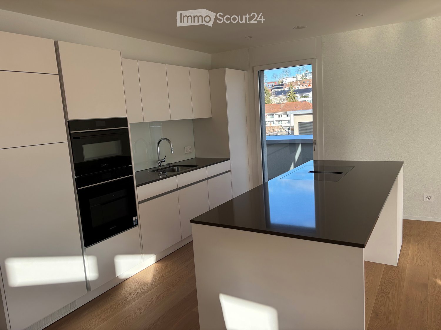 Modern kitchen with white cabinets, black countertops, a sink with a modern faucet, and an integrated oven. Large window offers a view of the city.
