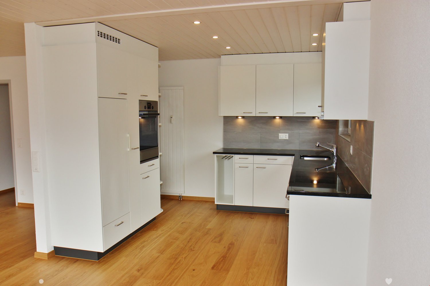 Modern kitchen with white cabinets, wooden flooring, stainless steel sink, and built-in oven.