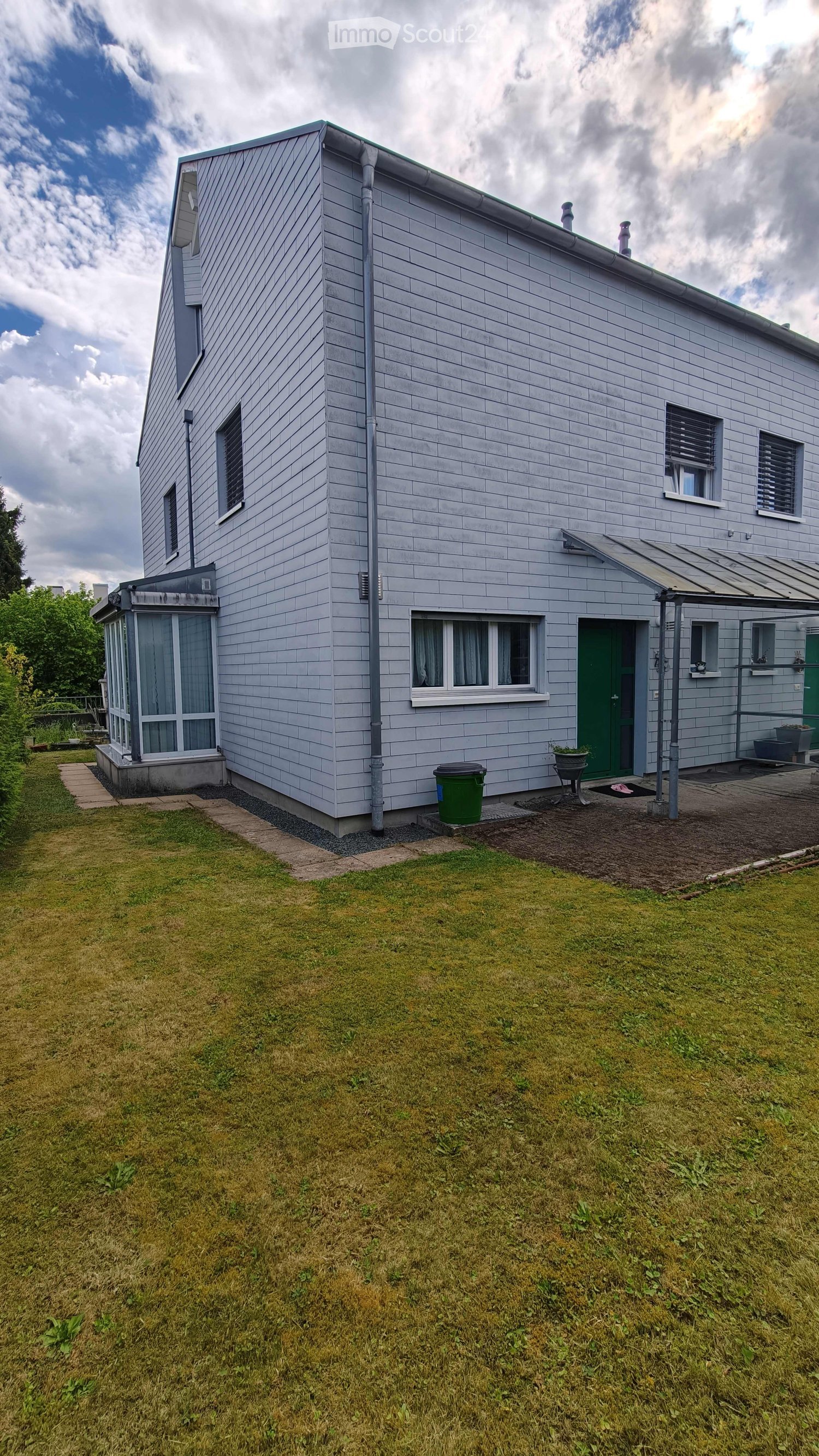 Two-story house with light gray siding, green front door, multiple windows, small porch, and a grassy yard.
