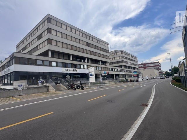 Multi-story commercial building with a storefront labeled "Biker's Life" and several motorcycles parked outside. The building has a modern design with large windows and a flat roof.