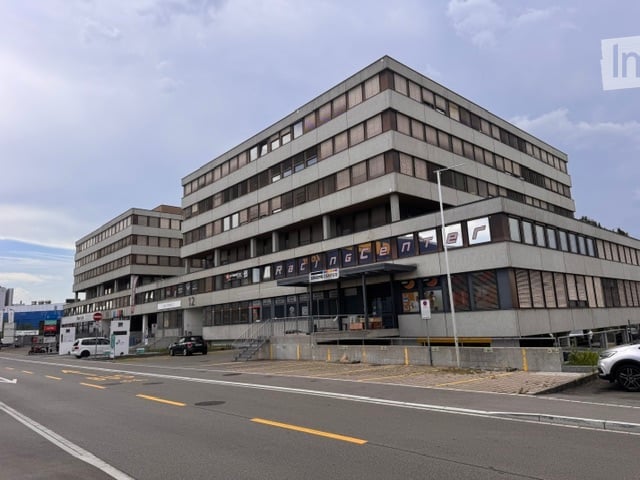 Modern multi-story building with a flat roof and large windows, featuring signage for "Razencenter" and a parking area in front.