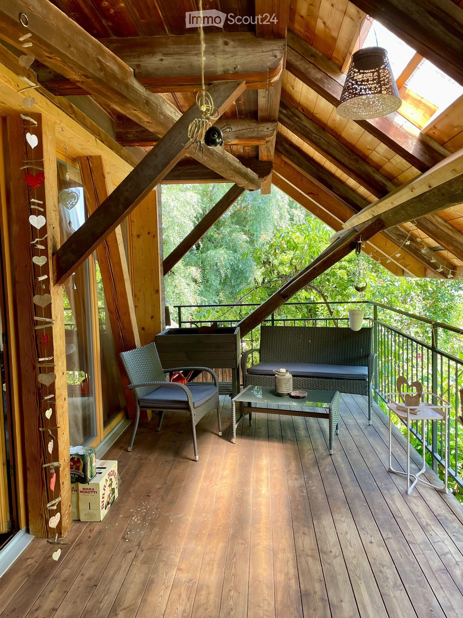 Wooden balcony with exposed beams, a sofa, chairs, a glass coffee table, and a hanging lamp.