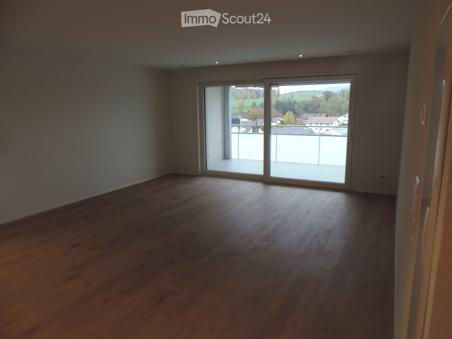Empty room with wooden flooring and large sliding glass doors leading to a balcony with a scenic view.
