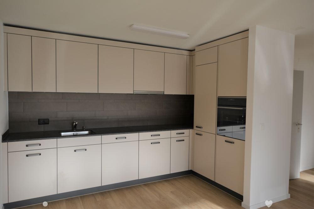 Modern kitchen with light-colored cabinets, black countertops, and a wooden floor. Features a sink and an oven.