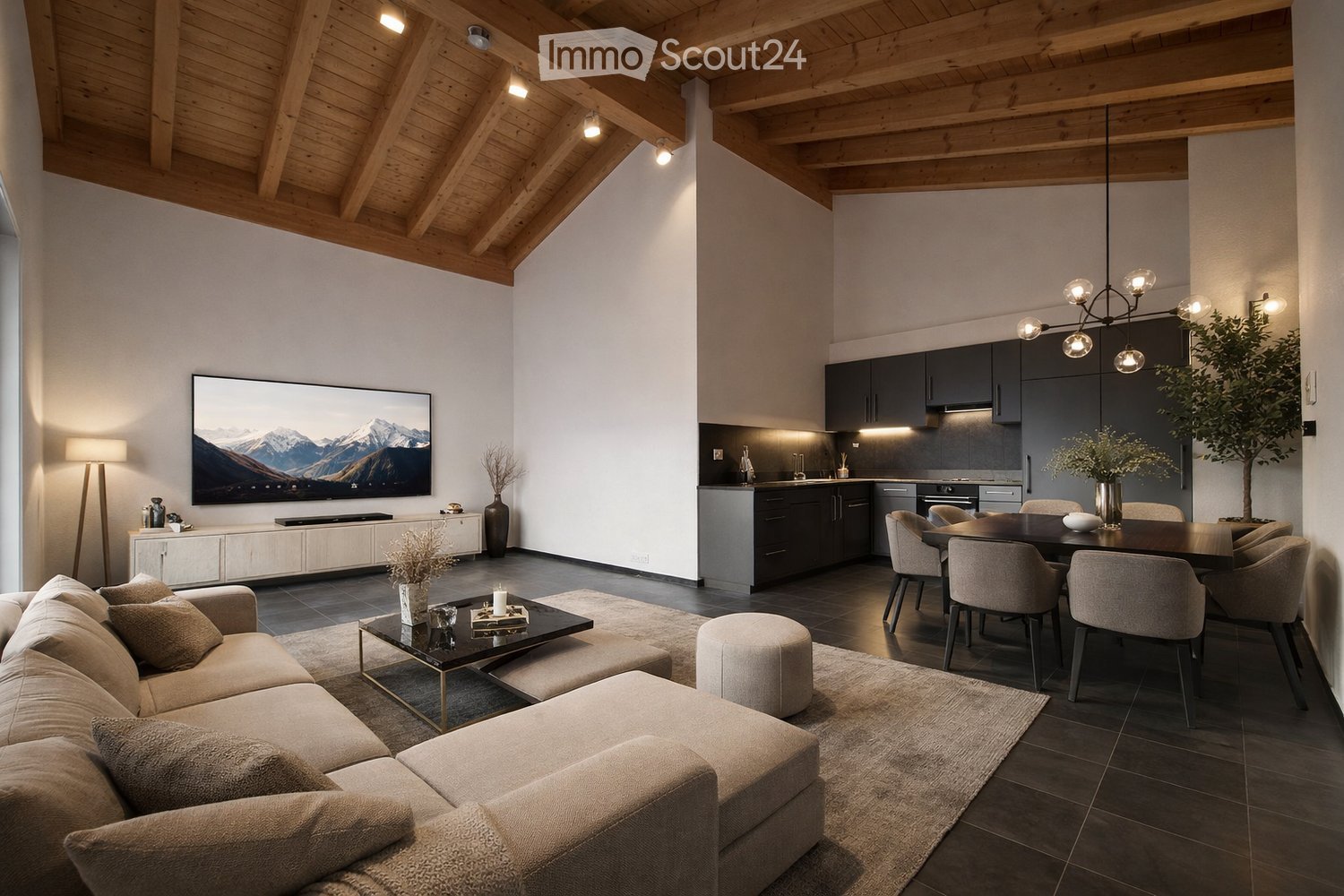 Open-concept living and dining area with a modern aesthetic. Features a large sectional sofa, coffee table, ottoman, dining table with chairs, and a sleek kitchen with dark cabinets and a central island. A large television is mounted on the wall, and the