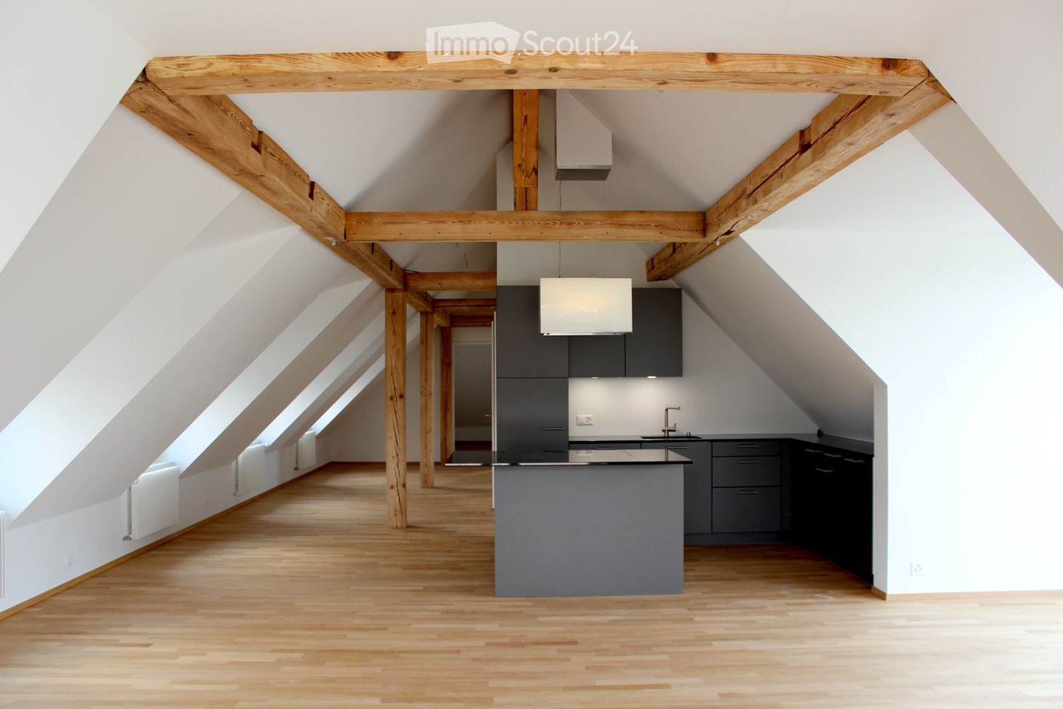Modern kitchen with wooden beams, light wooden flooring, grey cabinets, and a central island.