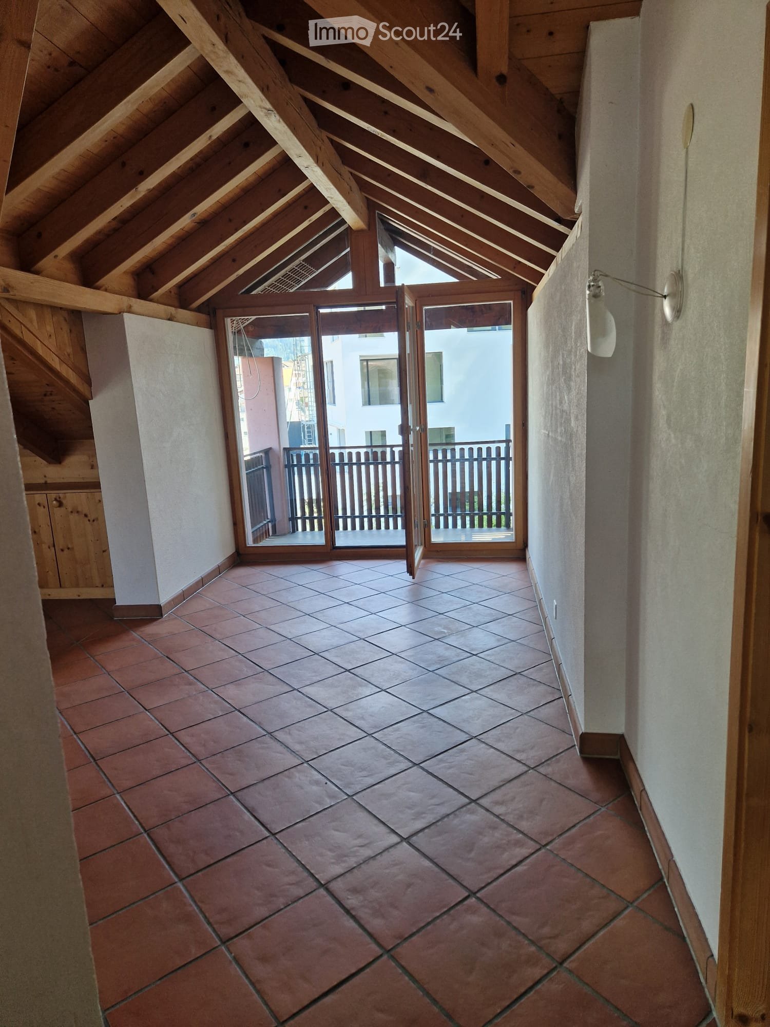 Spacious hallway with exposed wooden beams, terracotta tiled floor, and large sliding glass doors leading to a balcony.