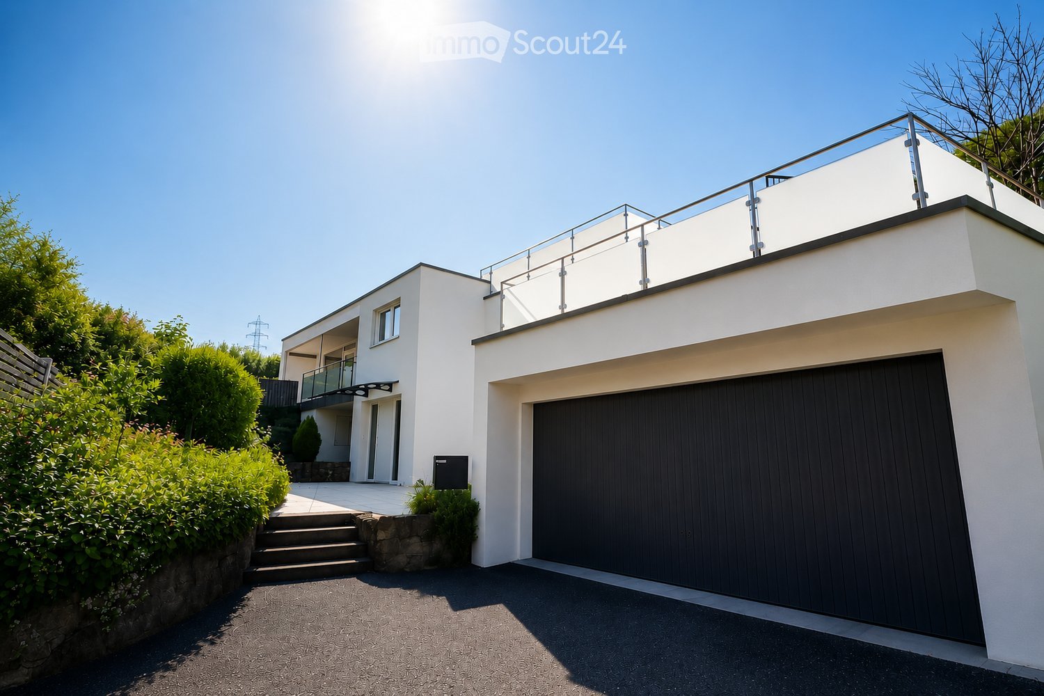Modern two-story house with white exterior, dark garage door, and a raised terrace with glass railing on the roof.