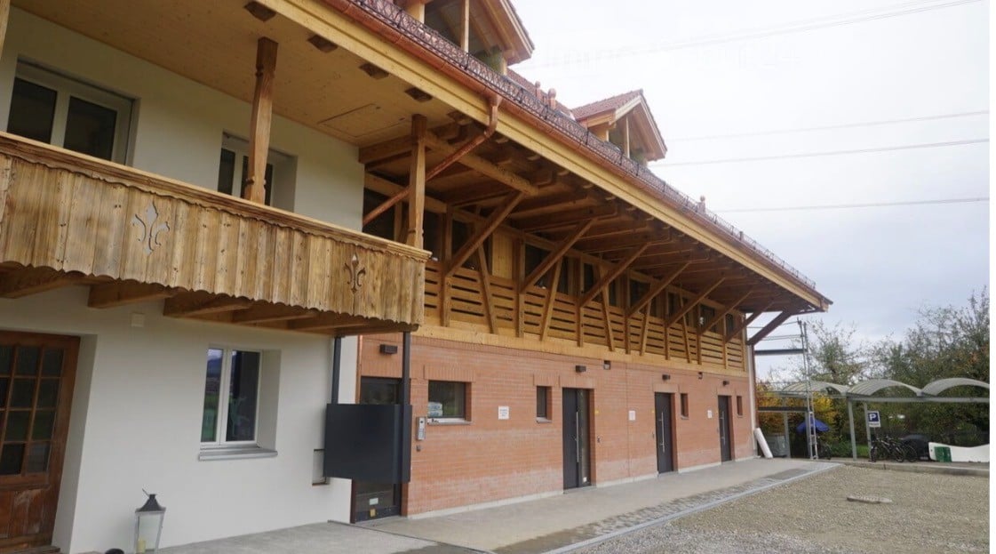 Two-story building with a wooden balcony and brick lower level, featuring multiple windows and doors.