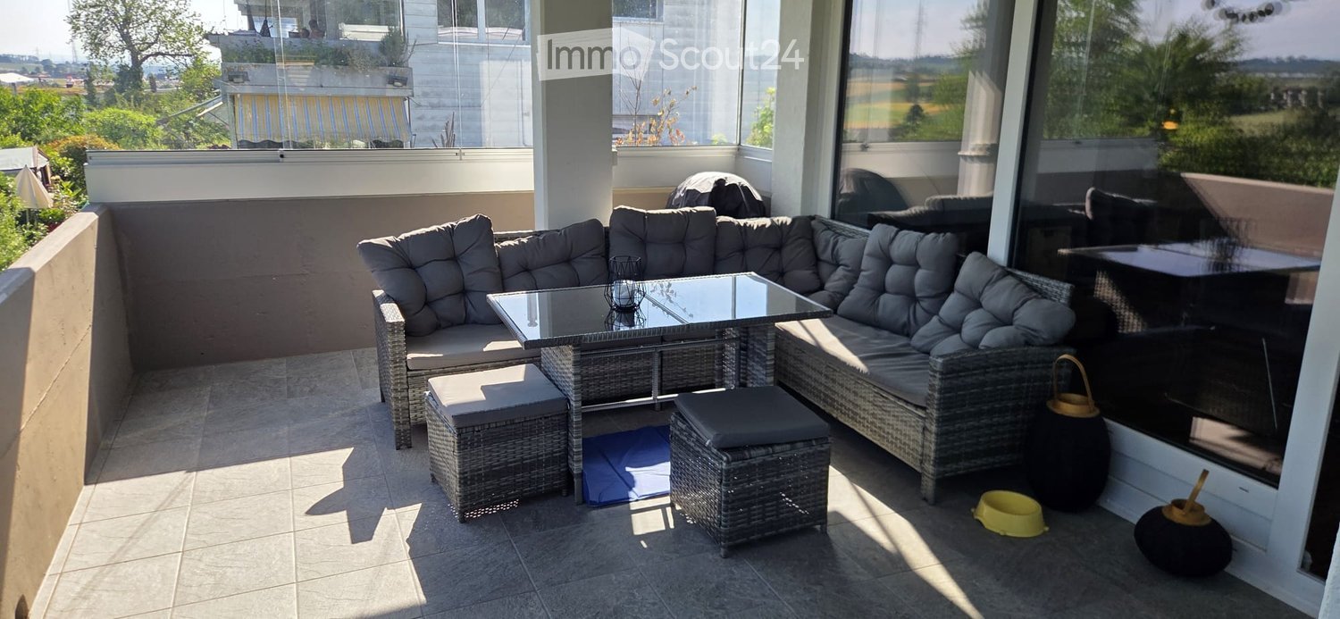 Balcony with wicker seating, glass coffee table, and outdoor view.