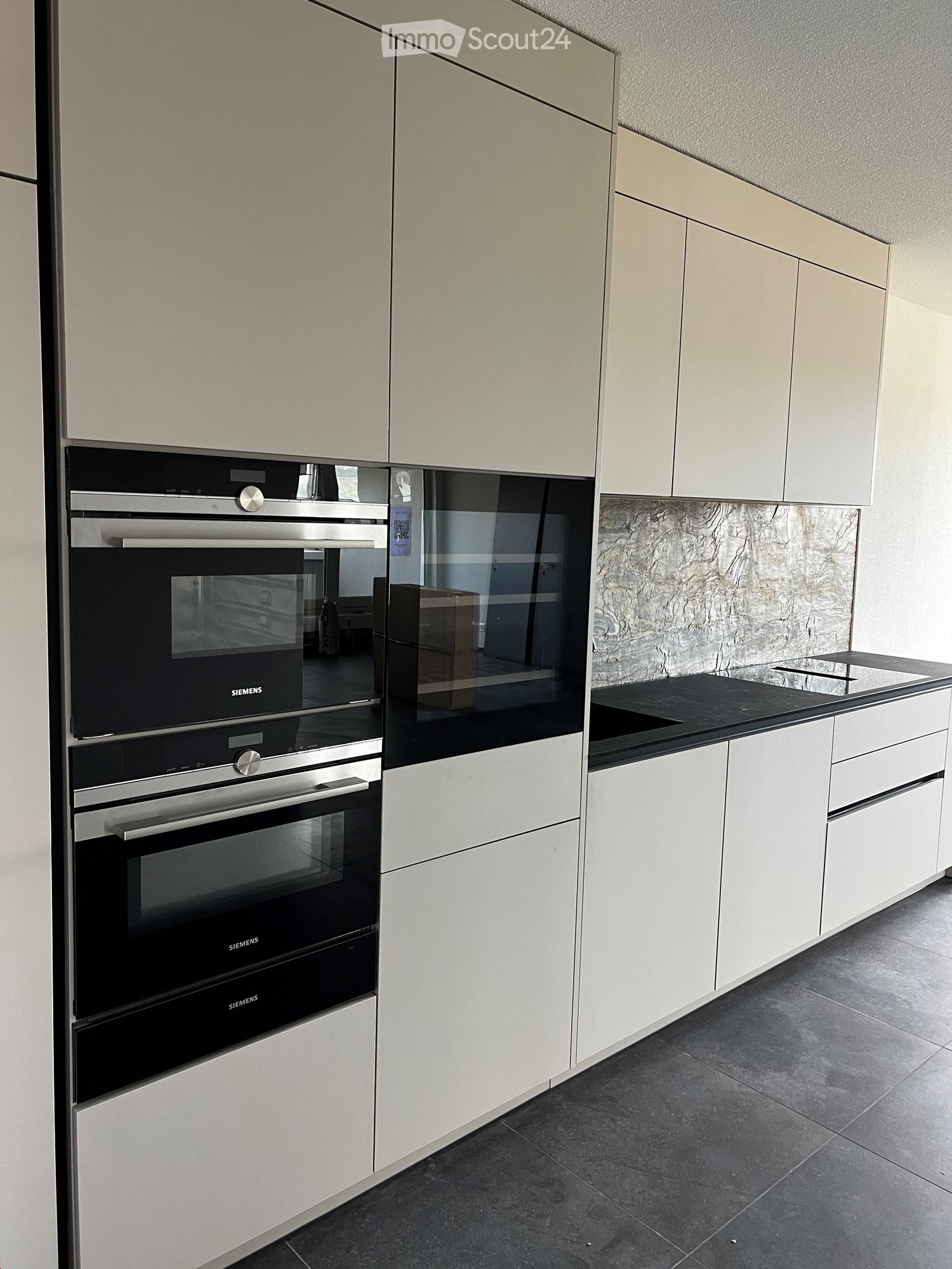 Modern kitchen with light-colored cabinets, stainless steel oven, and black countertop.