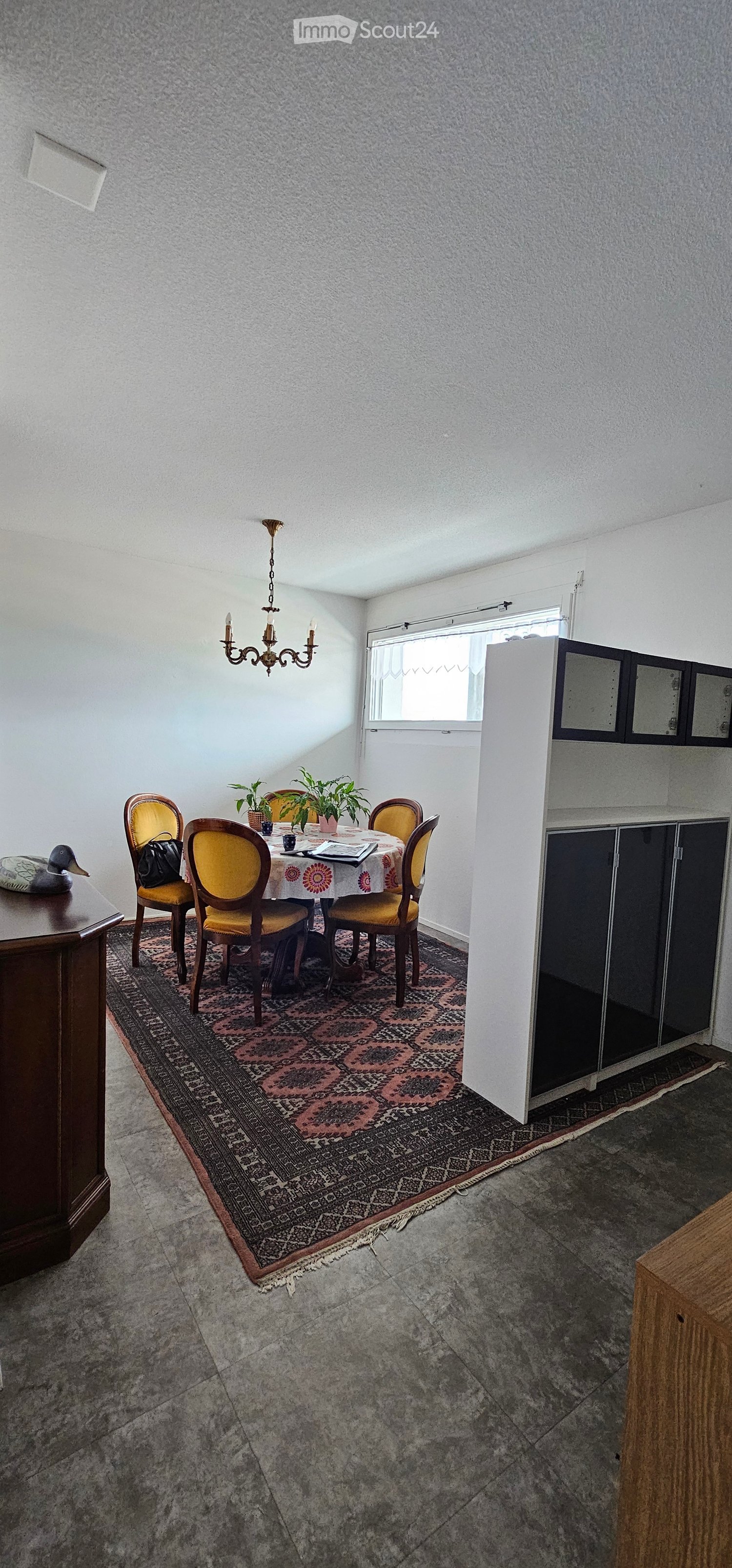 Dining area with a round table, six chairs, a chandelier, a cabinet, and a patterned rug.