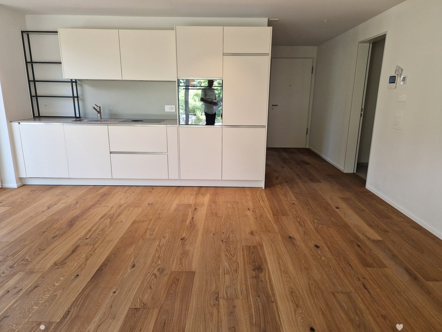 Modern kitchen with white cabinets, a sink, and a wooden floor. The space is clean and well-lit, with a visible doorway leading to another room.