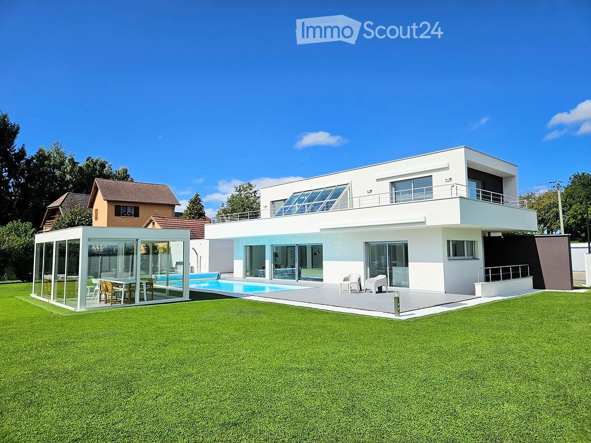 Modern two-story house with white facade, large windows, balcony, swimming pool, and outdoor seating area.