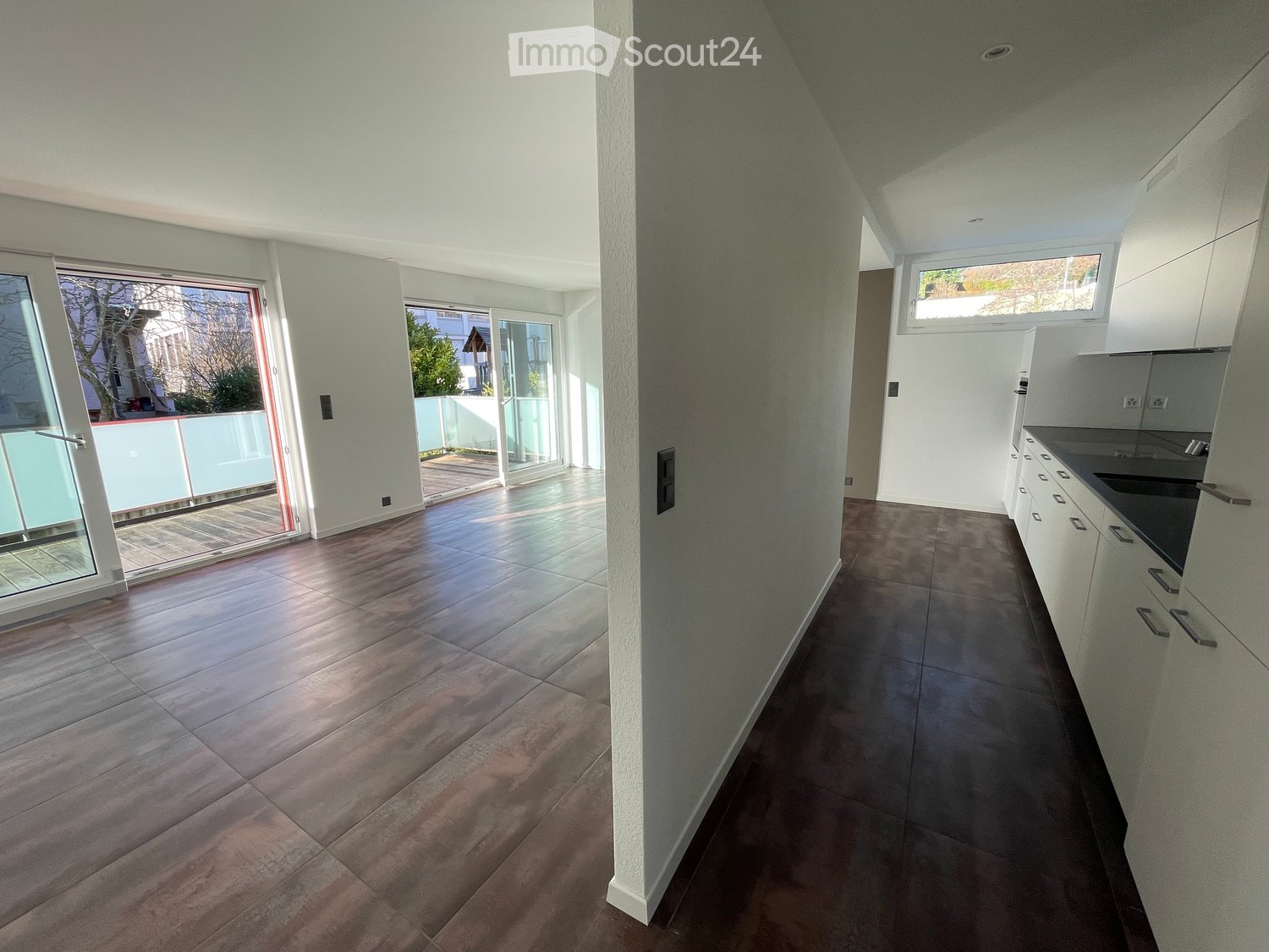 Empty room with tiled floor, white walls, and large windows leading to a balcony. The room is unfurnished and has a modern design.