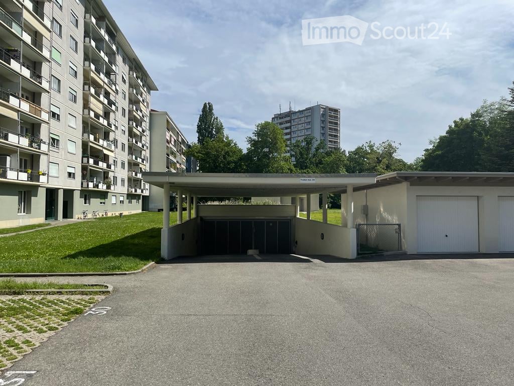 Multi-story residential building with a covered parking area and garage, surrounded by greenery.