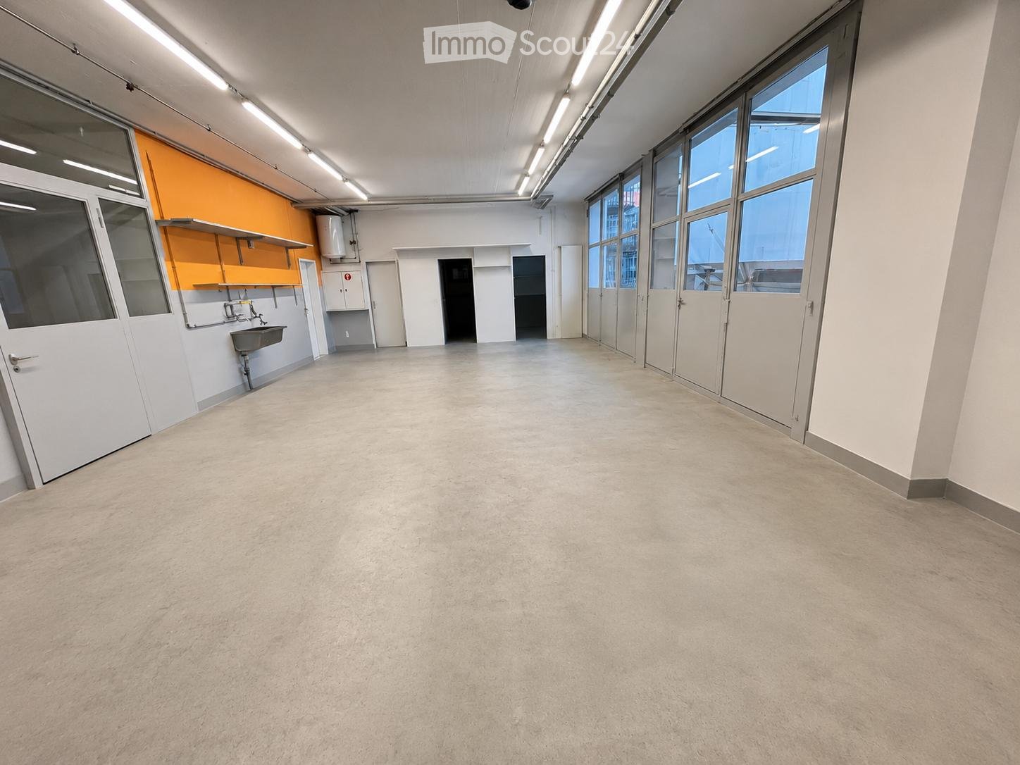 Empty room with white walls, large windows, and a sink area in the corner. No furniture or equipment present.