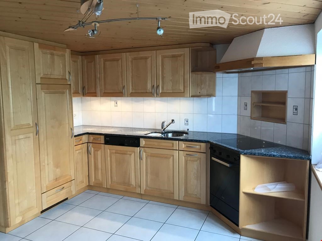 Bright kitchen with light wooden cabinets, white tiled walls, and a granite countertop. Features include a sink with a modern faucet, an oven, and a range hood.