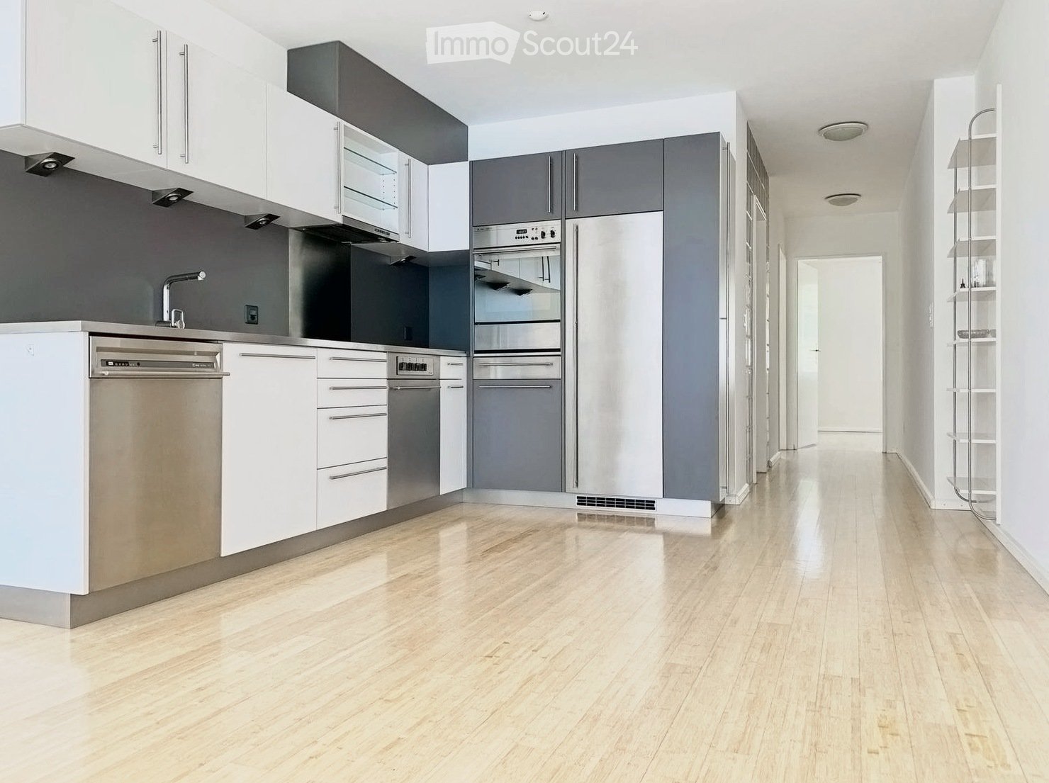 Modern kitchen with white and grey cabinets, stainless steel appliances, and light wooden flooring.