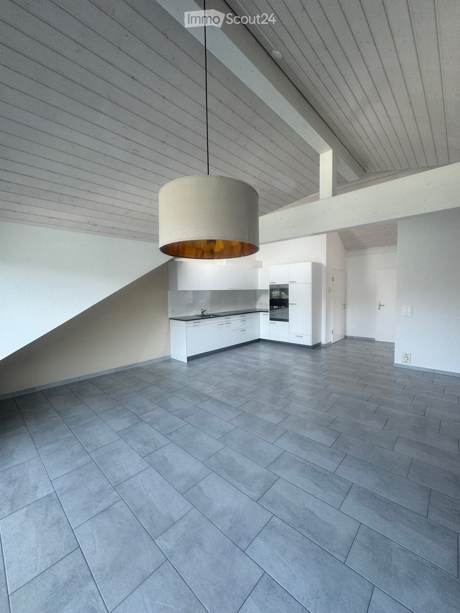 Modern kitchen with white cabinets, a central island, and a pendant light fixture. The space features a sleek, minimalist design with grey tiled flooring and a clean, open layout.