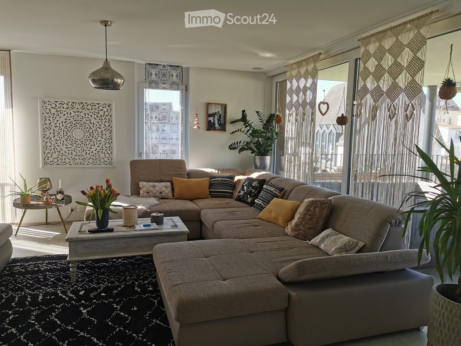 Modern living room with a large sectional sofa, coffee table, side table, pendant light, wall art, and plants.