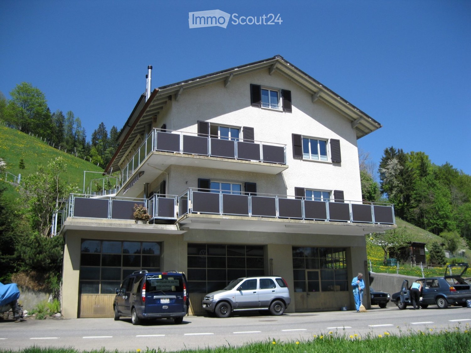Two-story house with white exterior, multiple windows, balconies, and a garage with several parked cars.