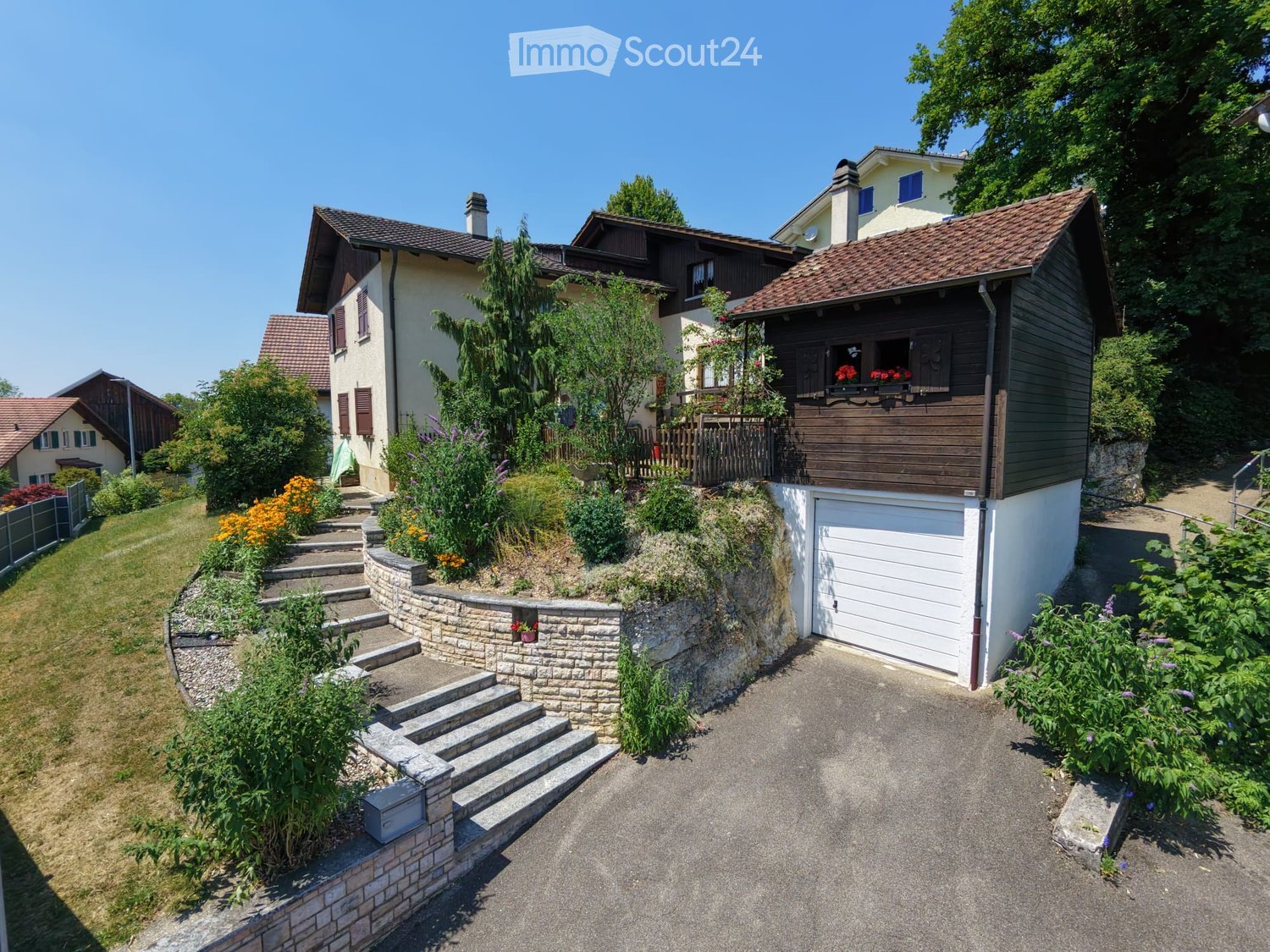 A two-story house with a brown tiled roof, white garage, and a landscaped garden with steps leading up to the house.