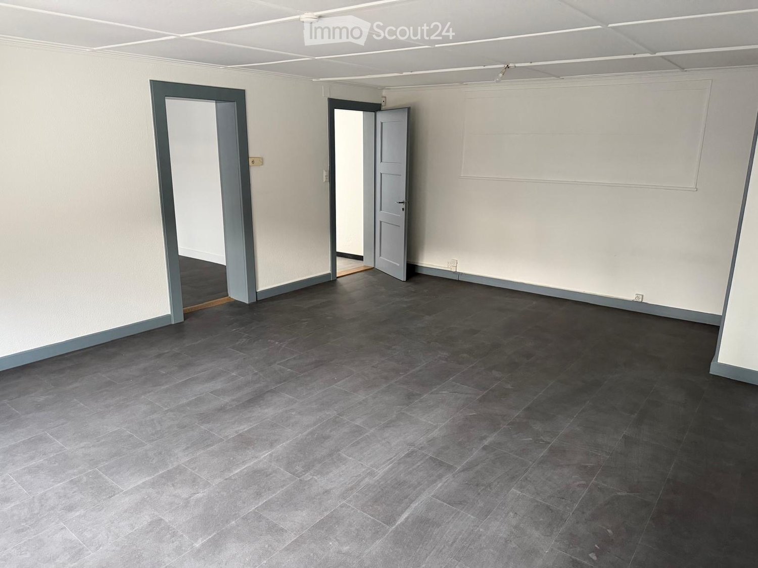 Empty room with grey tiled flooring, white walls, and two open doors leading to adjacent spaces.