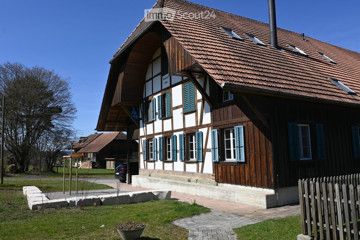 Traditional wooden house, brown roof, blue shutters, chimney, driveway, car parked, garden, wooden fence