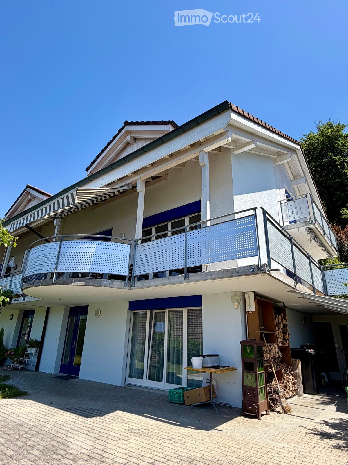 Two-story house with white exterior, blue shutters, balcony with metal railing, and outdoor patio area with a table and chairs.