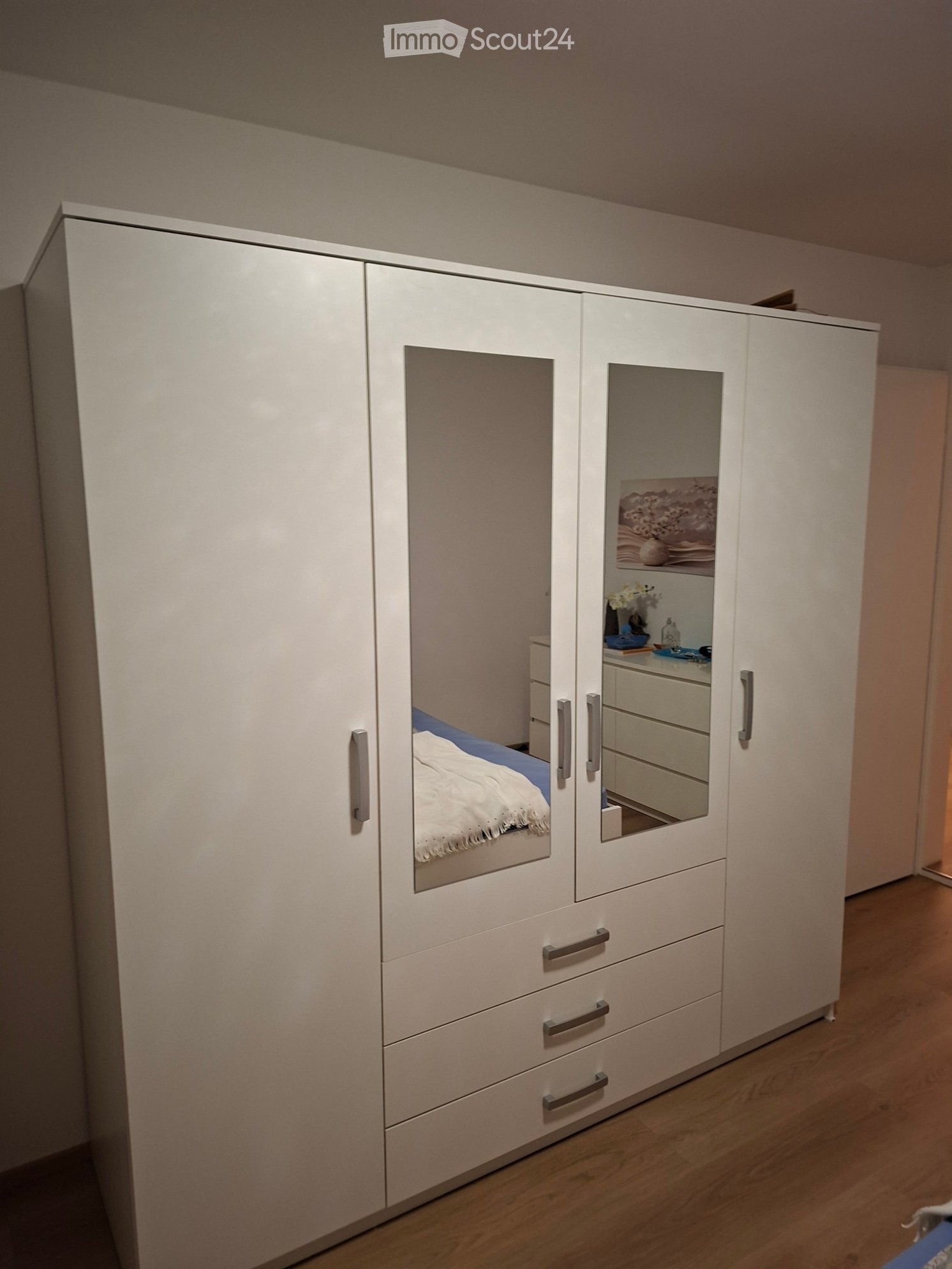 Modern bedroom with large white wardrobe, bed with blue bedding, nightstand, and mirror on the wardrobe door.