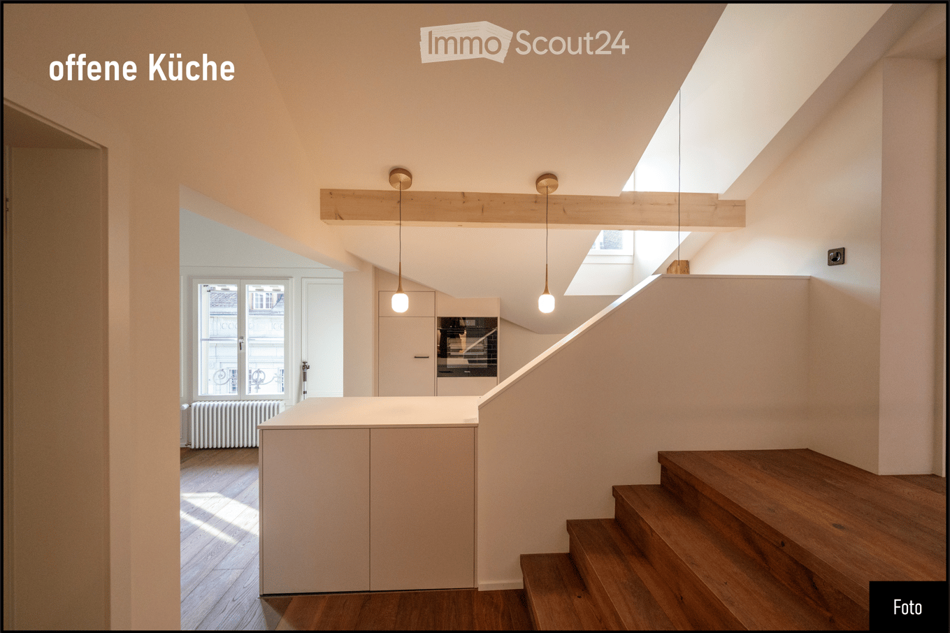 Open kitchen area with light-colored cabinets, wooden staircase, pendant lights, and large windows allowing natural light.
