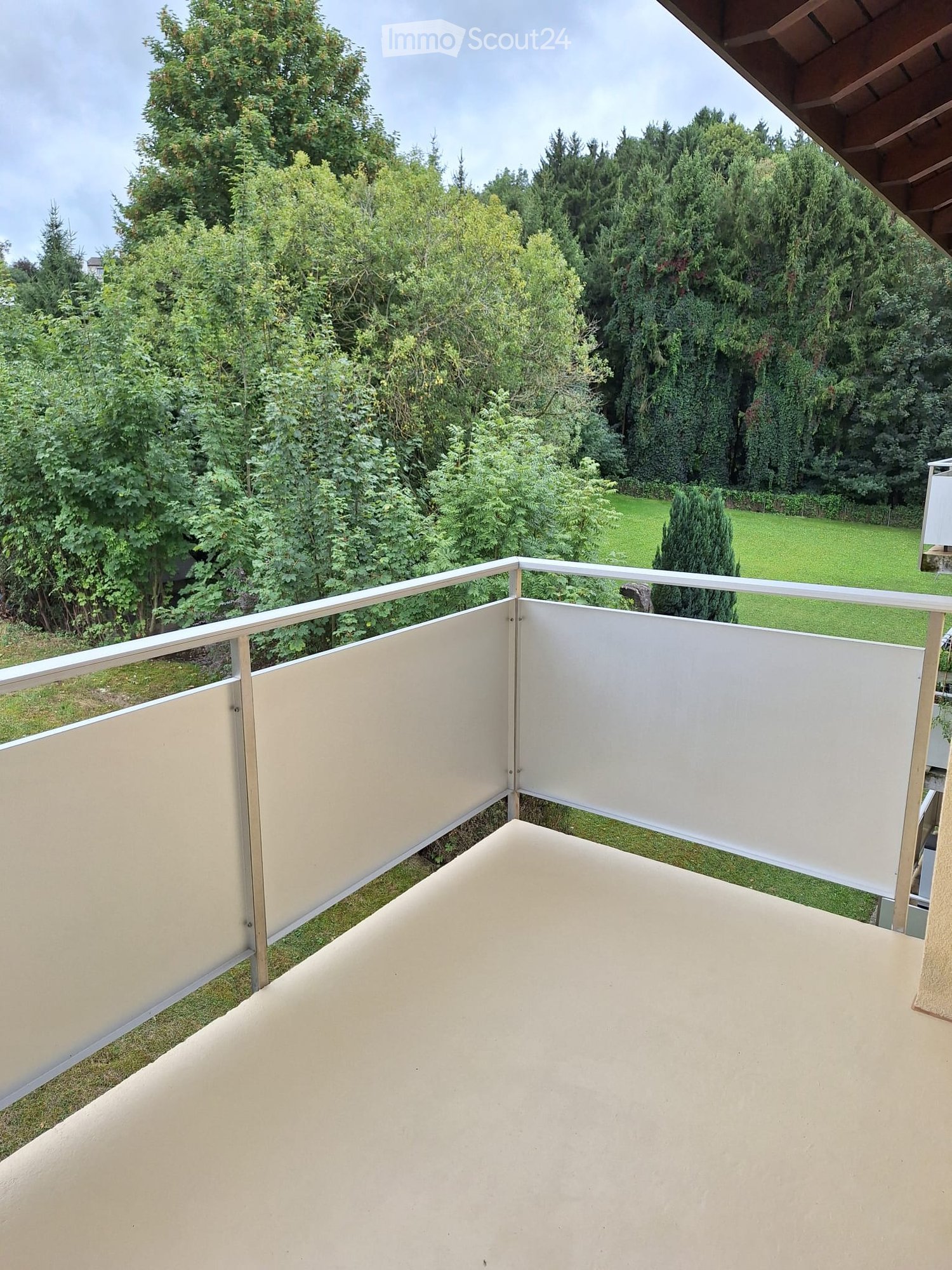 Balcony with white privacy screens, metal railing, and a view of a green garden and trees.