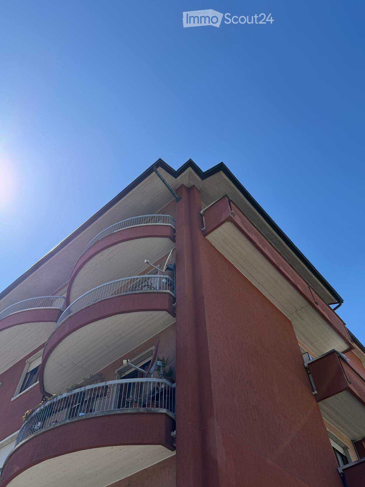Multi-story residential building with red brick facade, curved balconies, and metal railings.