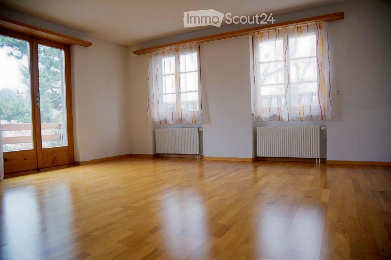 Empty room with wooden flooring, large windows with curtains, radiators, and a sliding glass door leading to a balcony.
