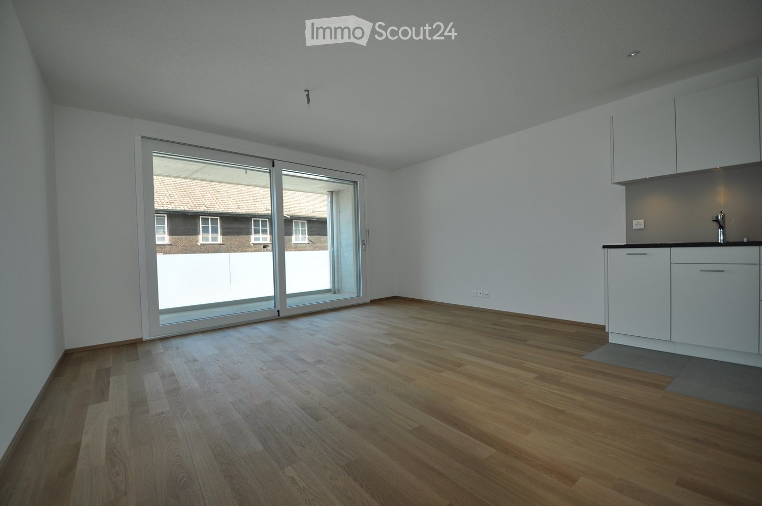 Empty room with wooden flooring, white walls, and a sliding glass door leading to an outdoor area. Minimalist design with built-in cabinets and a countertop on the right side.