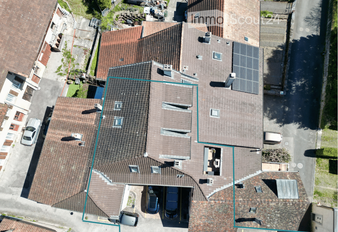 Aerial view of a multi-story residential building with a tiled roof, solar panels, and a garage with multiple parked cars.
